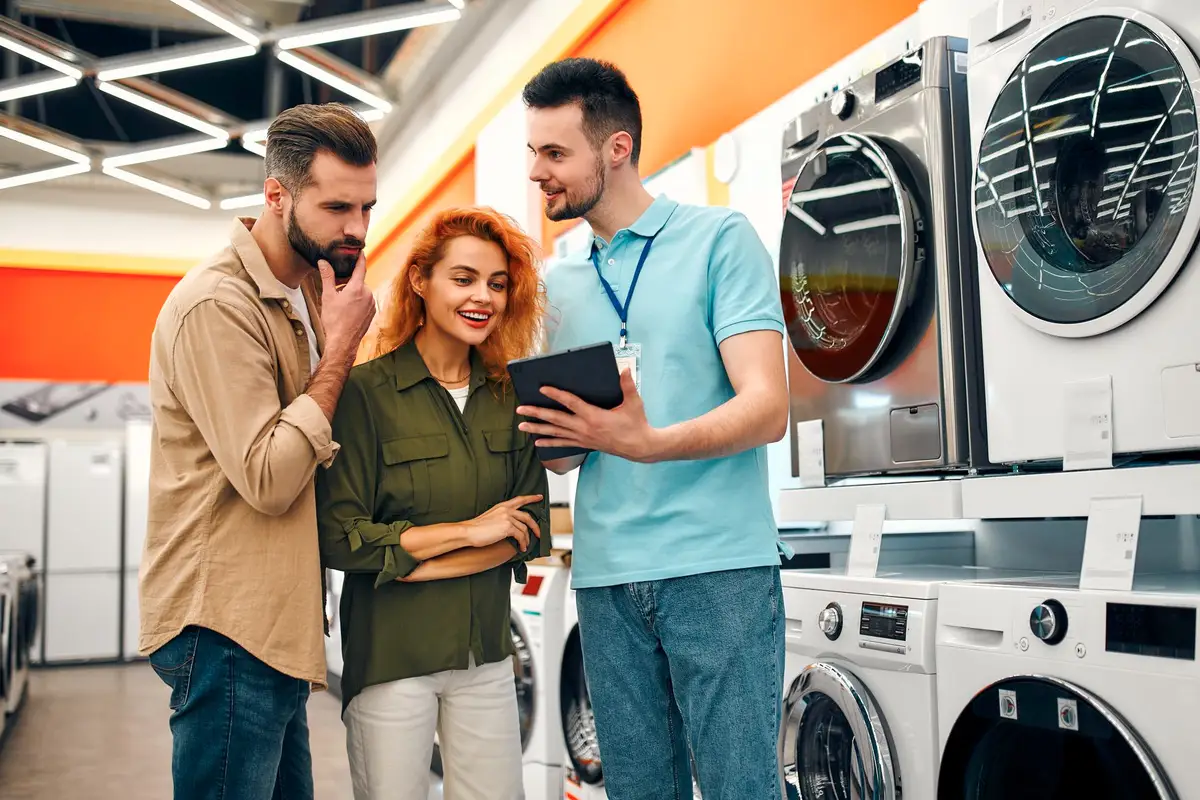 Personne comparant les étiquettes énergie d’un réfrigérateur et d’un lave-linge dans une cuisine lumineuse