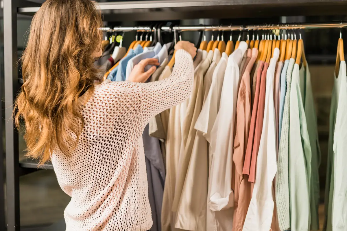 Dressing en bois clair avec vêtements sobres et colorés, chaussures rangées et personne choisissant une tenue