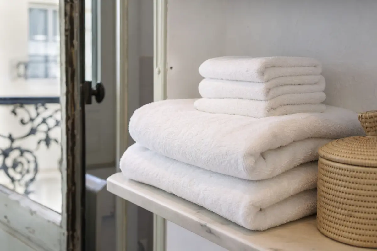 Serviettes de toilette blanches pliées et empilées sur une étagère de salle de bain, lumière naturelle douce
