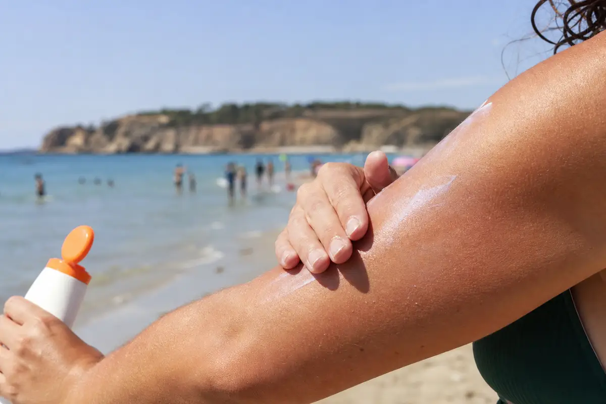 Crème solaire appliquée sur un bras bronzé avec un léger voile blanc visible, lumière naturelle d’été en bord de mer