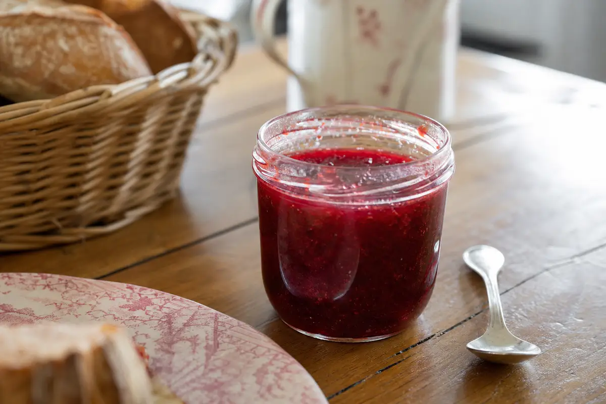 Pot de confiture ouvert avec une cuillère propre posée à côté sur une table en bois, lumière naturelle du matin
